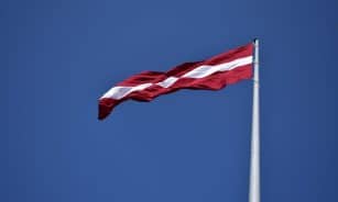 Vibrant Latvian flag flying on a flagpole against a clear blue sky, symbolizing national pride.