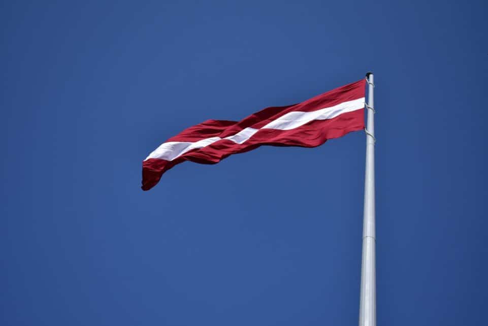 Vibrant Latvian flag flying on a flagpole against a clear blue sky, symbolizing national pride.