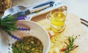 Close-up of herb-infused oil preparation with rosemary and garlic on a wooden board.