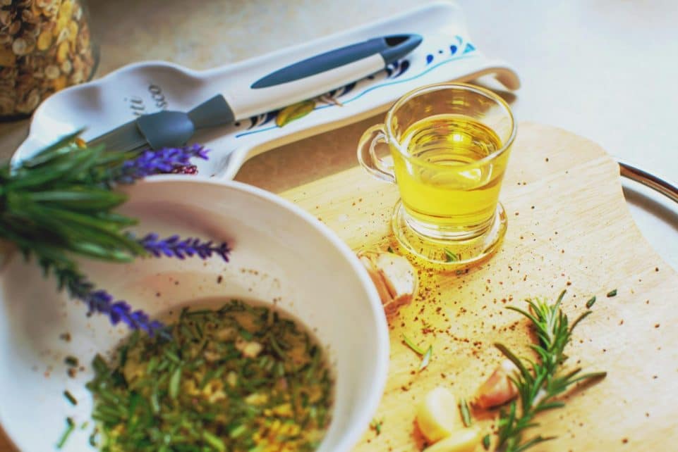 Close-up of herb-infused oil preparation with rosemary and garlic on a wooden board.