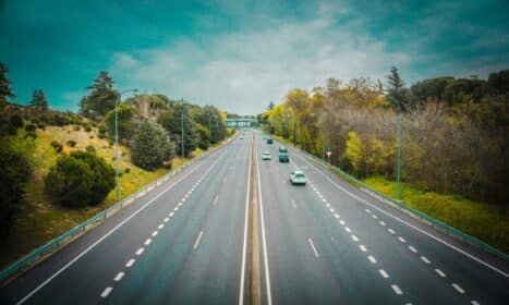 Aerial view of an open highway surrounded by trees and clear skies, perfect for travel.