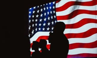 Silhouettes of people against a waving American flag, symbolizing unity and patriotism.
