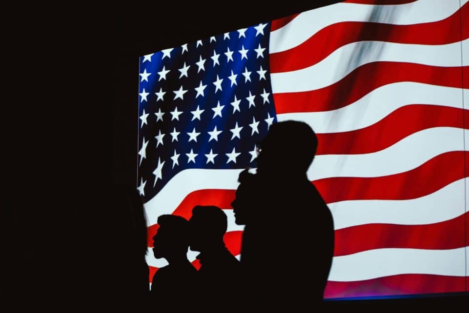 Silhouettes of people against a waving American flag, symbolizing unity and patriotism.