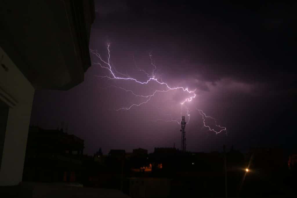 A striking lightning storm illuminates the night sky above silhouetted city buildings.