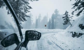 A car drives through a foggy snow-covered mountain road, capturing winter's serene beauty.