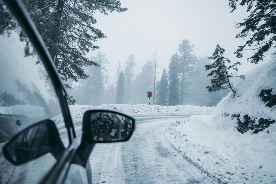 A car drives through a foggy snow-covered mountain road, capturing winter's serene beauty.