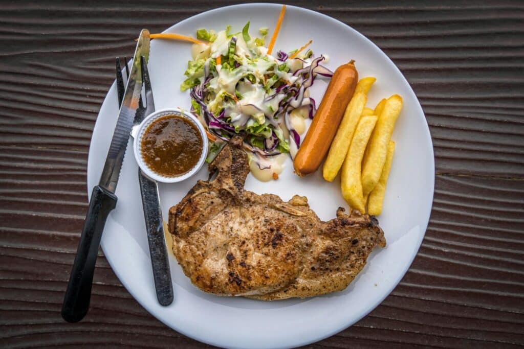 Delicious grilled pork chop with vibrant salad, fries, and sauce on a ceramic plate.