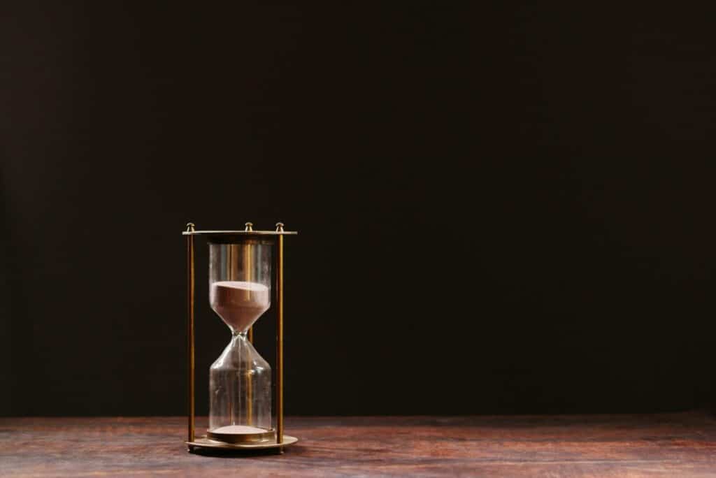 A classic hourglass with sand trickling down, symbolizing the passage of time, against a dark background.