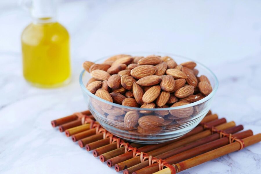 Close-up of almonds in a glass bowl next to a bottle of oil on a bamboo mat.