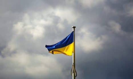 A Ukrainian flag waves prominently against a dramatic cloudy sky, symbolizing resilience.