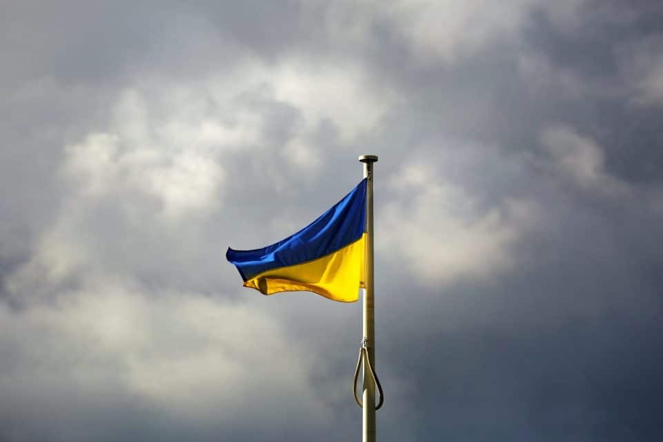 A Ukrainian flag waves prominently against a dramatic cloudy sky, symbolizing resilience.