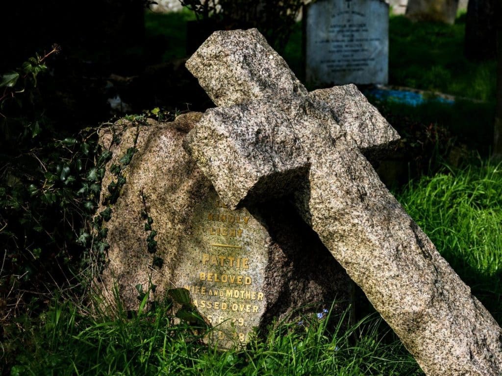 A serene cemetery scene featuring a weathered stone cross and gravestone overgrown with lush grass.