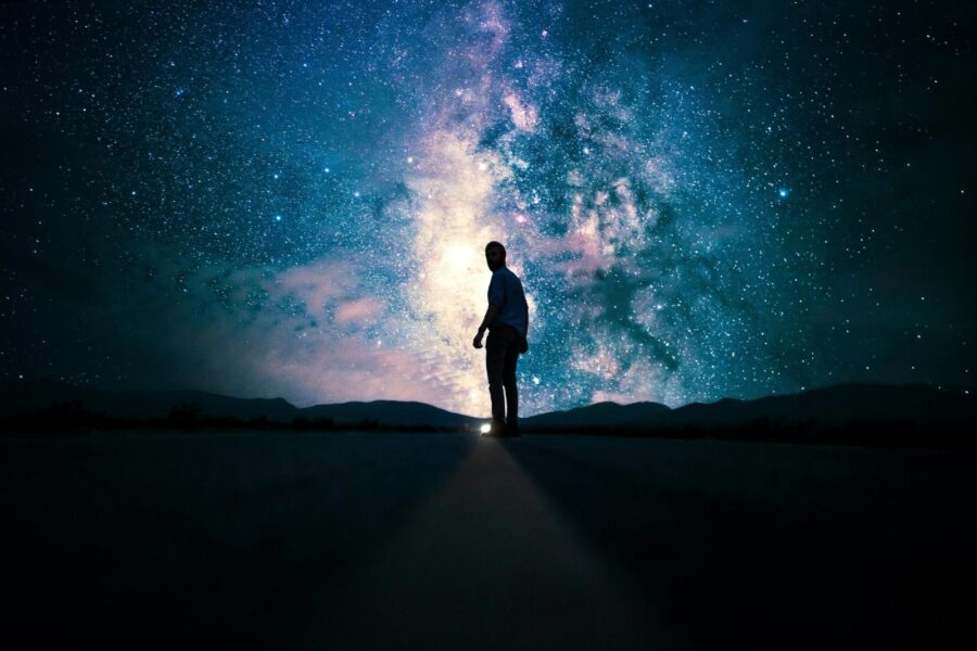 Silhouette of a man standing on a road, gazing at a stunning star-filled night sky with the Milky Way.