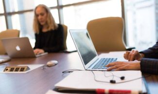 Colleagues collaborating in a bright, modern office setting, focused on laptop work.