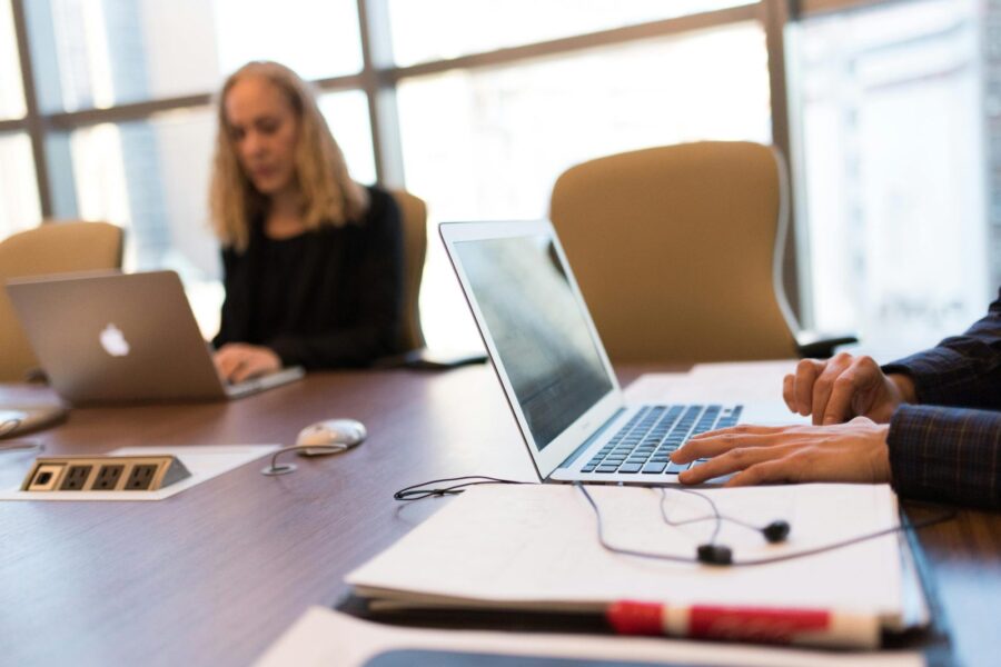 Colleagues collaborating in a bright, modern office setting, focused on laptop work.