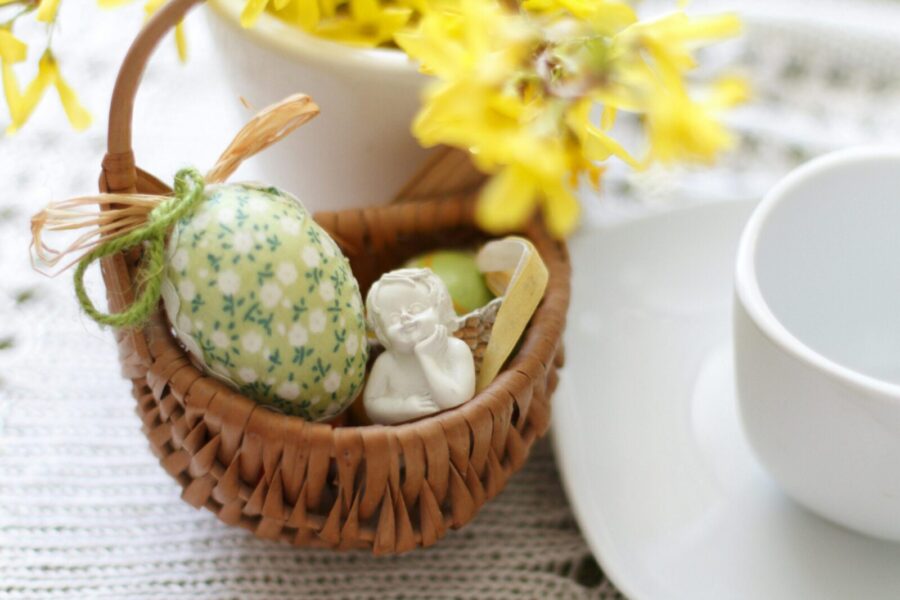 Charming Easter basket with a floral egg and angel figurine, surrounded by yellow flowers.