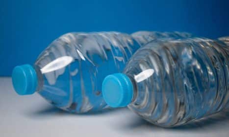Close-up of clear plastic water bottles with blue caps on a blue background.