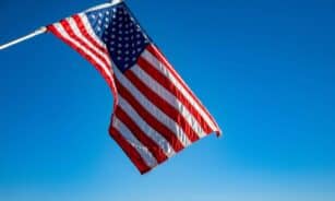 The American flag proudly waves on a flagpole against a clear blue sky, symbolizing freedom and patriotism.