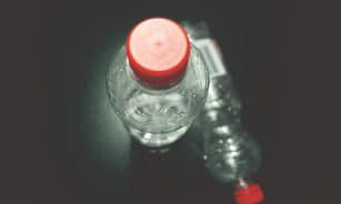 Top view of two clear plastic bottles with red caps on a dark surface, highlighting recycling.
