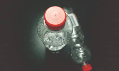 Top view of two clear plastic bottles with red caps on a dark surface, highlighting recycling.