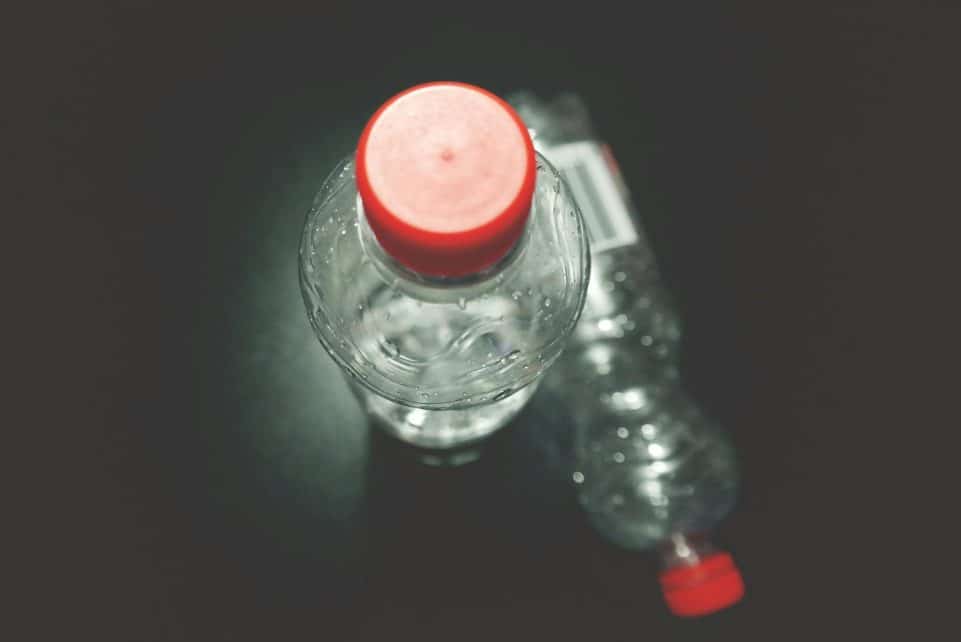 Top view of two clear plastic bottles with red caps on a dark surface, highlighting recycling.