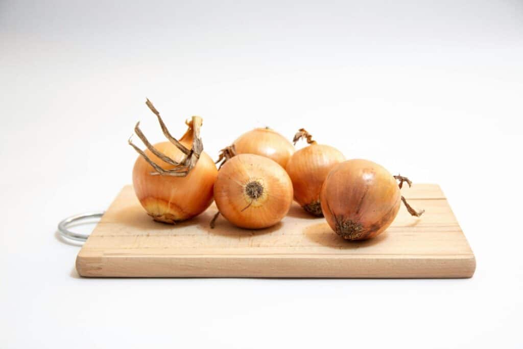 Five fresh onions neatly arranged on a wooden cutting board against a white background.