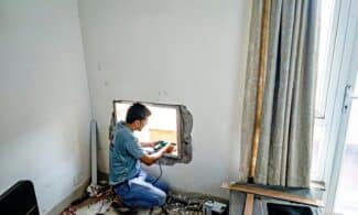 A man uses a drill to fit a window on an indoor construction site, focused on renovation work.