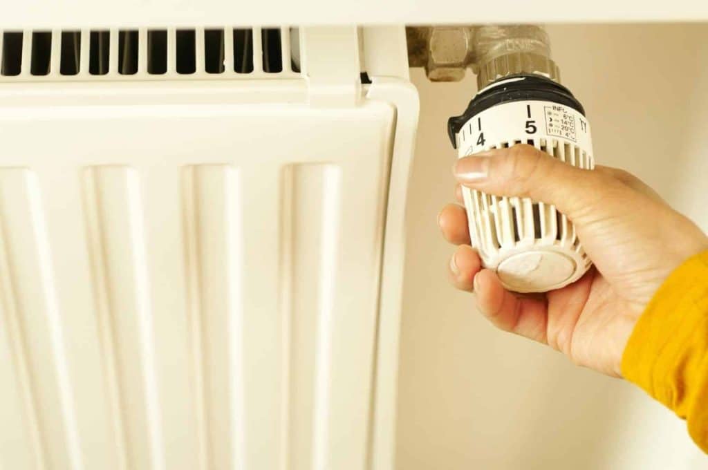 Close-up of hand adjusting radiator thermostat to control home heating temperature.