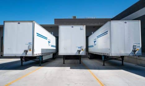 Three white cargo trailers parked at an industrial shipping dock under clear blue skies.