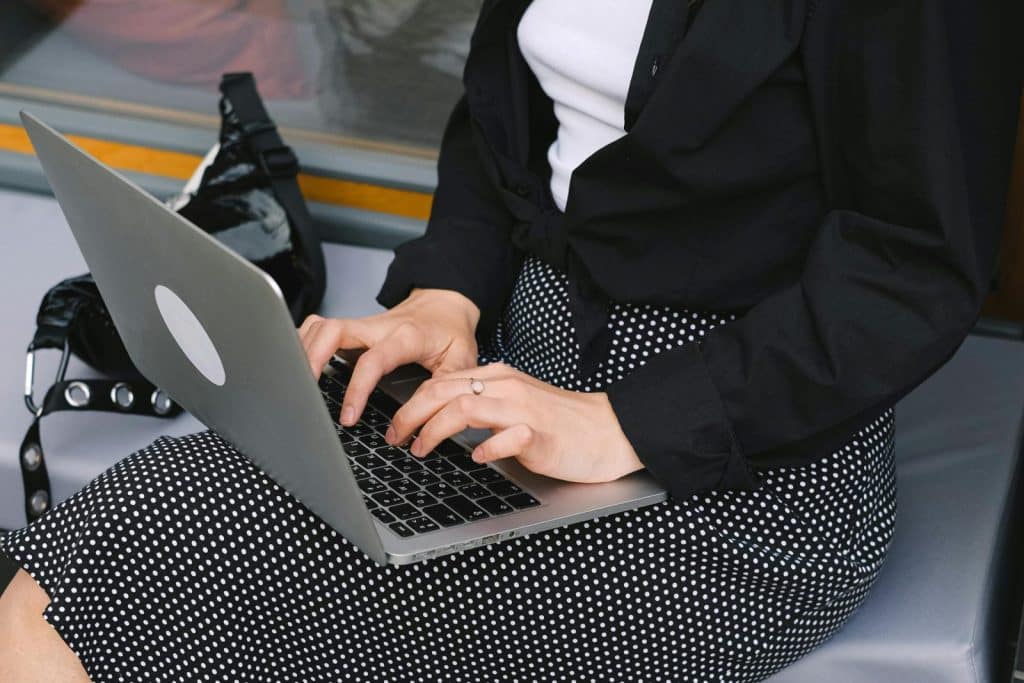 Close-up of a woman typing on a laptop, wearing a black polka dot skirt, seated on a bench.