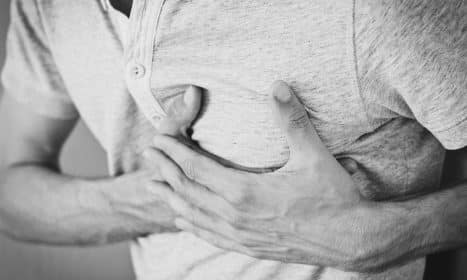 Black and white photo of a man clutching his chest, indicating discomfort or pain.