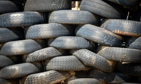 Pile of black rubber tires stacked outdoors in daylight.