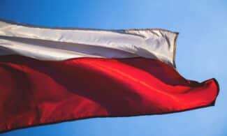 Close-up of a Polish flag waving against a clear blue sky, symbolizing patriotism and national pride.