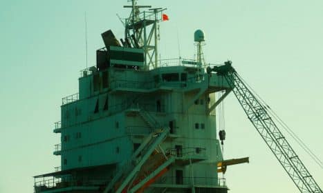 Close-up of an industrial ship's structure and crane against a sunset backdrop.