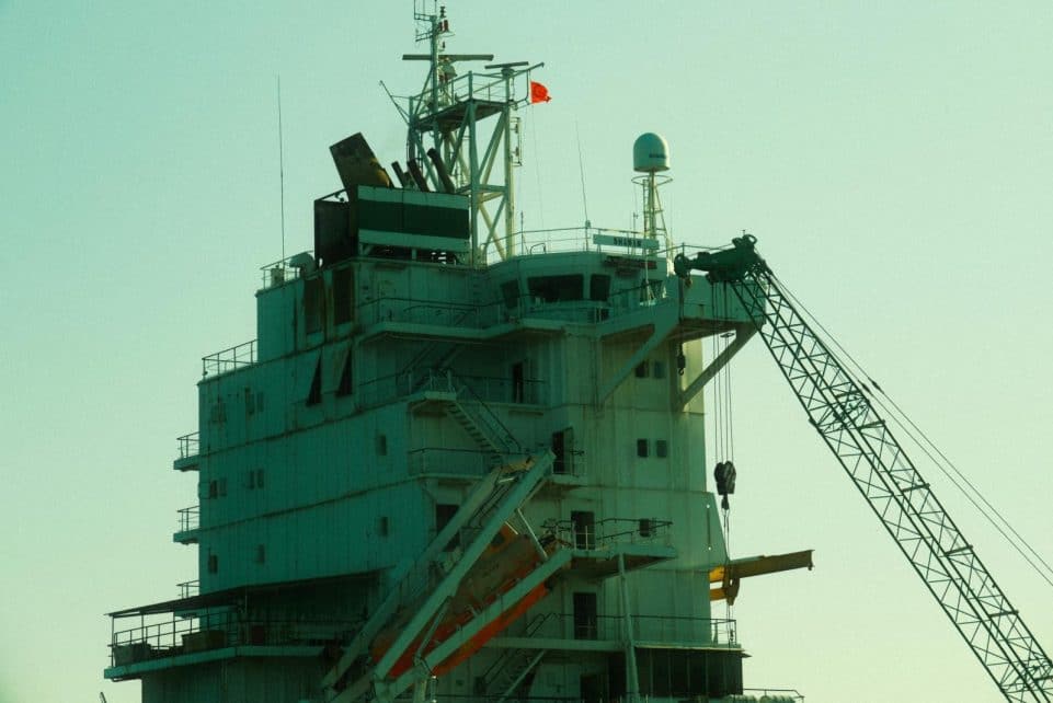 Close-up of an industrial ship's structure and crane against a sunset backdrop.