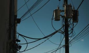 Low angle view of power lines and transformers against a clear blue sky, depicting modern electricity infrastructure.