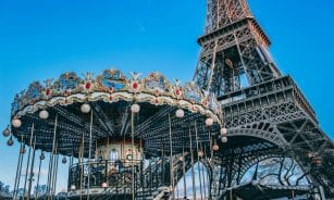 Eiffel Tower with a classic carousel in foreground on a bright day in Paris, France.