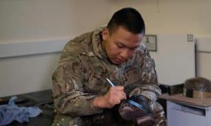A British soldier is polishing boots indoors, showcasing military routine and discipline.