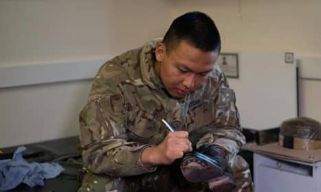 A British soldier is polishing boots indoors, showcasing military routine and discipline.