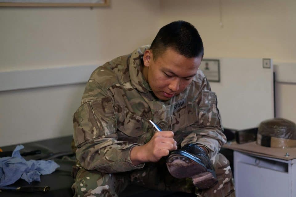 A British soldier is polishing boots indoors, showcasing military routine and discipline.