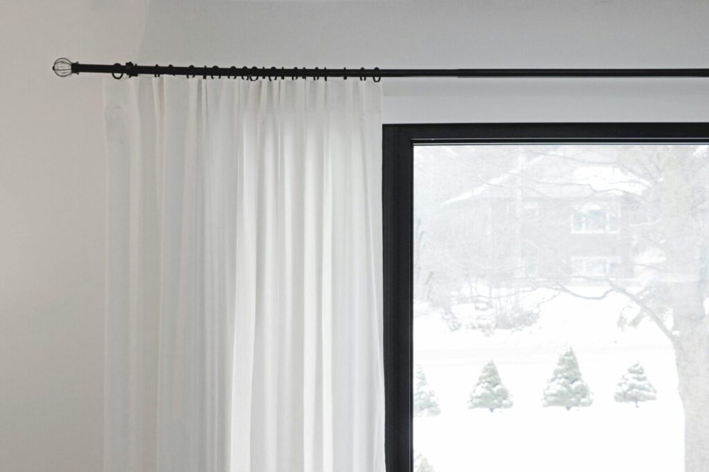 White curtains partially covering a window with a snowy outdoor view. Minimalist home decor.