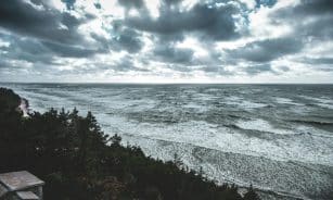 A dramatic view of the Baltic Sea coastline in Latvia with moody skies and waves crashing on the shore.