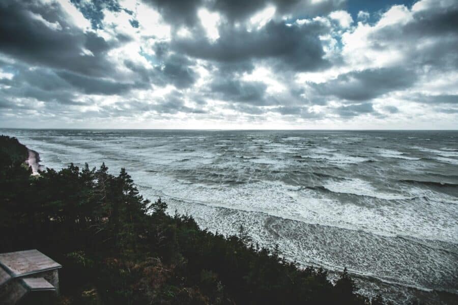 A dramatic view of the Baltic Sea coastline in Latvia with moody skies and waves crashing on the shore.