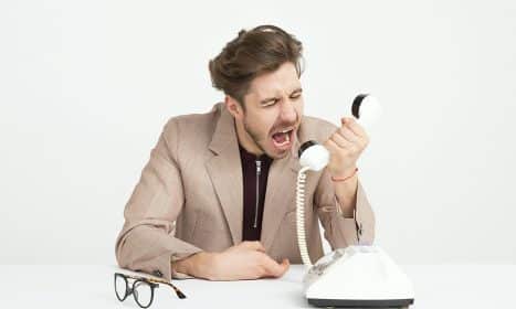 Businessman in a beige suit shouting into a vintage telephone, expressing frustration at work.