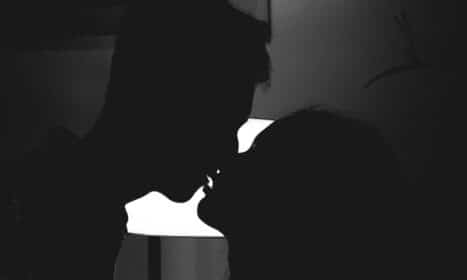 Silhouette of a couple kissing in a romantic and intimate moment against a bright light.