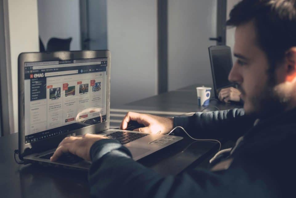 Adult man using laptop to browse an online marketplace in a modern office.