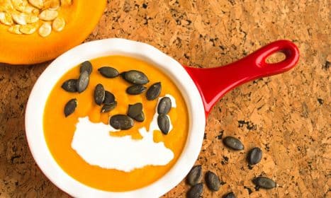 Appetizing close-up of pumpkin soup with cream and seeds in a red bowl.