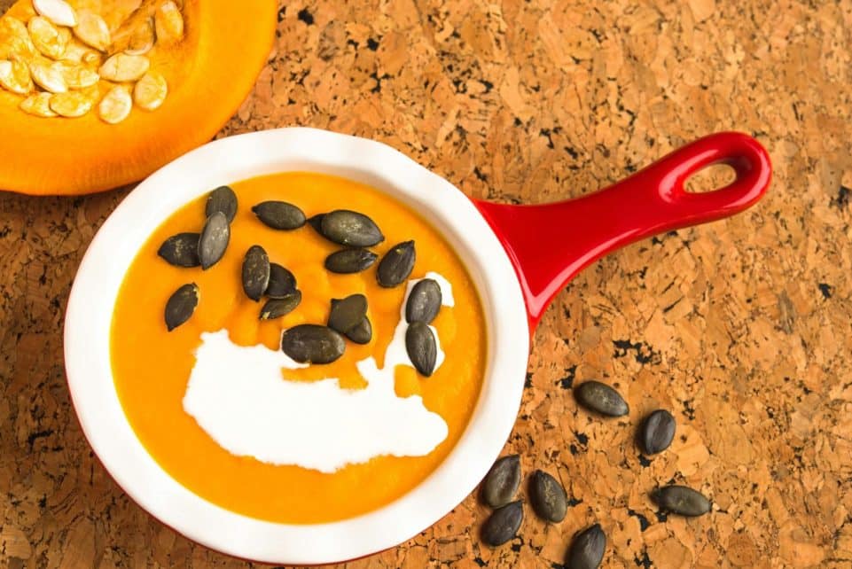 Appetizing close-up of pumpkin soup with cream and seeds in a red bowl.