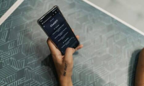 Close-up of a person holding a smartphone displaying the ChatGPT application interface on a patterned table.