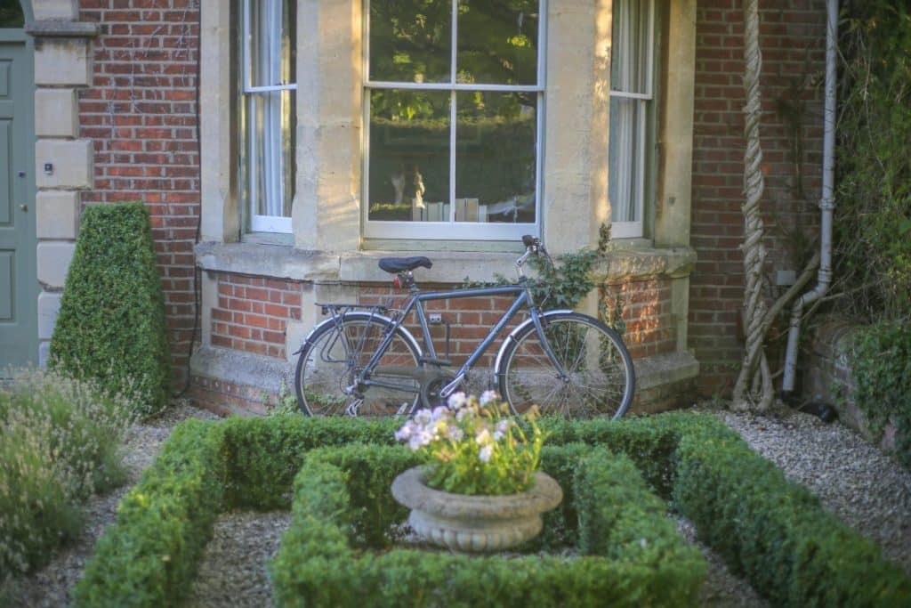 A bicycle leans against a brick house with a lush garden, ideal for serene outdoor living.
